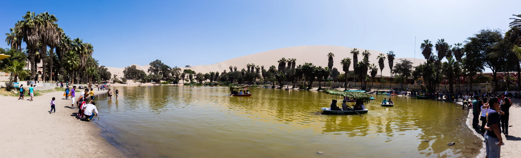 Huacachina lagoon with palms and visitor buildings along its shore